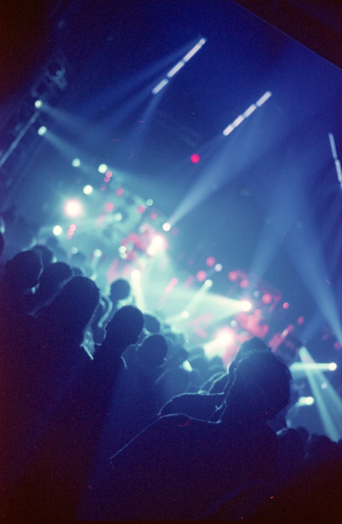 Silhouetted crowd watching a brightly lit stage with blue and white spotlights at a concert.