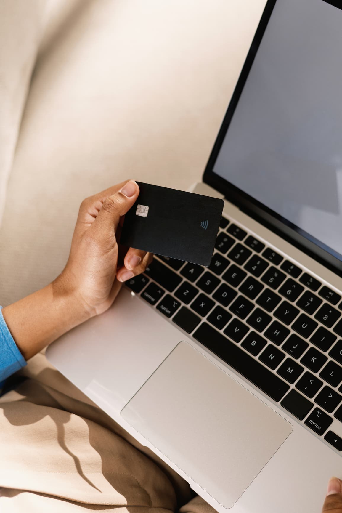 Hand holding a black contactless credit card above a laptop keyboard.
